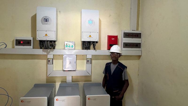 Technician standing beside wall-mounted inverters and batteries